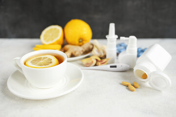 Cold and flu season treatment still life with cup of tea, lemon, pills, thermometer, nasal sprays, garlic and ginger, health and wellness concept