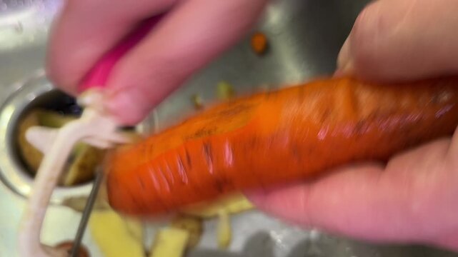 Close-up of a hand peeling a carrot with a vegetable peeler over the sink