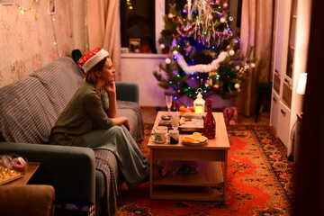 A young woman in a red New Year's hat celebrates Christmas alone at home
