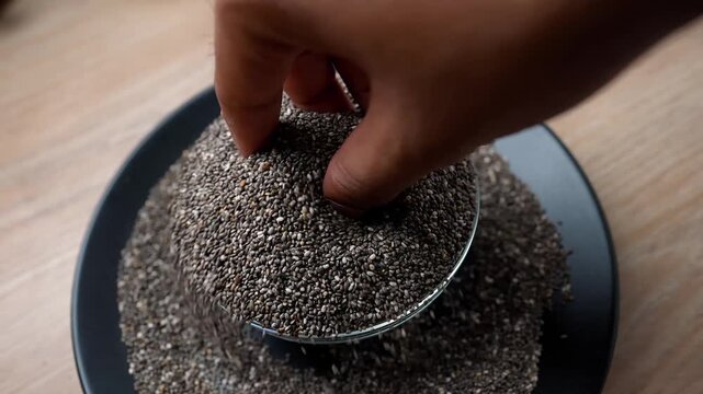 Hand picking chia seeds from a bowl on a wooden table