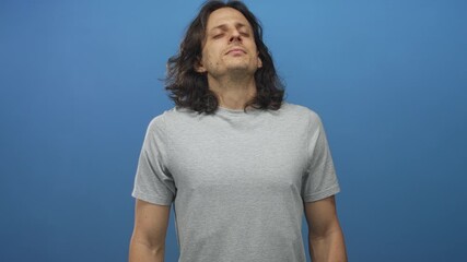 Man with eyes closed and head tilted back wearing grey t shirt in blue studio; serenity introspection.