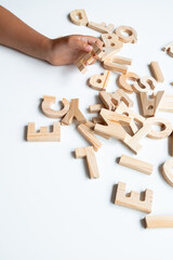 Child hand arranging wooden alphabet letters on white surface