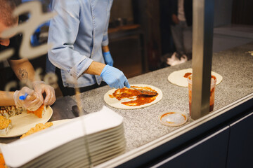Chef preparing a delicious pizza with tomato sauce at a busy pizzeria location
