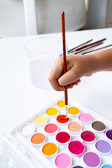 Child painting with watercolors on white desk inside bright room