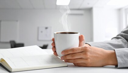 hands holding plain coffee cup over planner with empty boxes soft window light minimal workspace