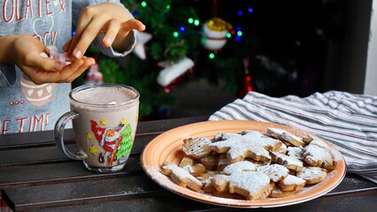 Children’s Hands Holding Marshmallows for Hot Cocoa – Cozy Christmas Scene with Biscuits and Tree Background