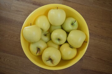 A large yellow plastic container filled with ripe yellow apples