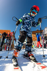 Scenic portrait view kid beginner skier close-up take on ski boots downhill ski slope piste bright warm morning sunrise sky background.  Mountain landscape winter resort