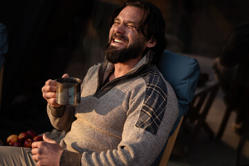 Man enjoying a warm drink while sitting outdoors in a cozy setting at sunset