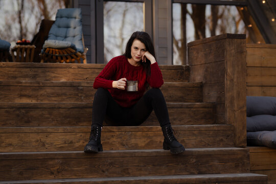 Woman enjoying a warm drink while sitting on wooden steps in a cozy outdoor setting during autumn