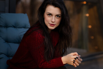 Young woman seated indoors with dark hair and striking expression during evening