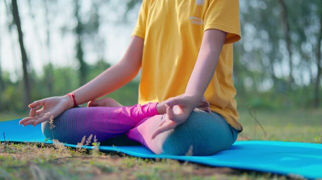 In the morning sunlight a woman sitting in lotus position on a yoga mat in nature, close up shot, India.