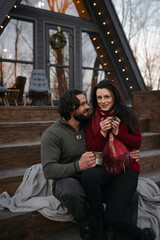 Couple enjoys warm drinks on porch of cozy cabin during chilly evening
