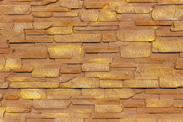Close up of decorative stone fence made of rectangular textured stones in warm brown and golden tones, ideal for use in architecture, construction, and design backgrounds.
