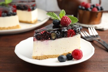 Piece of delicious cheesecake with berries and mint served on wooden table, closeup