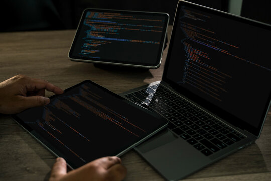 Programmer writing Development Website design code at a desk with laptop and tablet dark workspace, hands on keyboard, CSS and HTML modern software development, tech projects.