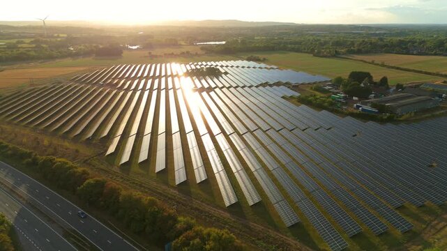 Aerial view of vast solar panel field reflecting the sunlight near a road, with green trees and fields, Leicester, England, United Kingdom.