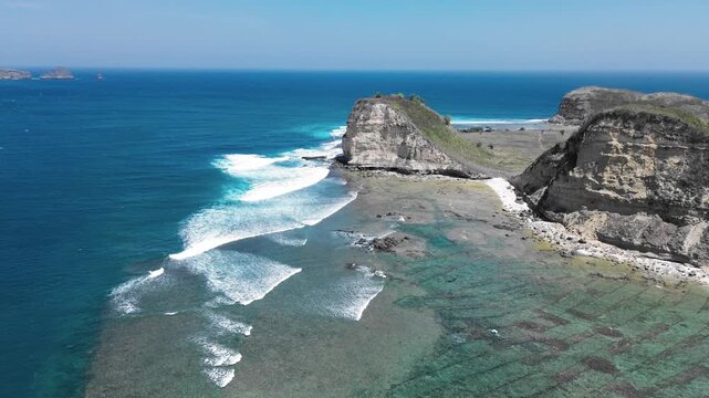Stunning aerial shot of a remote tropical coastline where turquoise ocean waves break against majestic cliffs on a sunny day. Mawun beach Lombok Indonesia.
