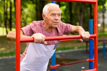 Elderly man doing fitness on sports ground equipment in park