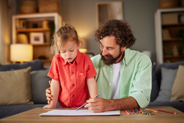 Naklejka premium A father and his young child focus on drawing together at home. The child stands by the table, excitedly creating art while the father guides and supports lovingly.