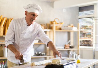 Mature experienced baker weighs pieces of raw dough on scales for making croissants