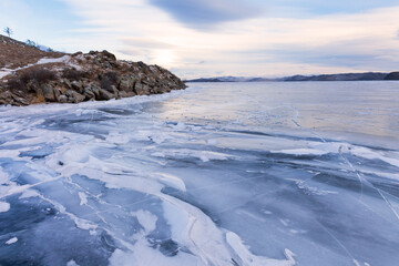 Obraz premium Baikal Lake at December sunset. Beautiful winter landscape with frozen Small Sea and Kurkut bay. View of blue ice with cracks and snow near rocky coast. Natural background. Winter travels