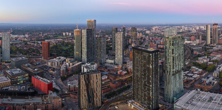 Aerial panorama of Manchester skyline at sunrise with warm morning light and clear pastel sky.
