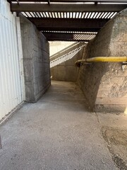 Concrete pedestrian underpass with industrial elements and yellow pipe, urban structure in harsh daylight