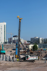 A sunny day at a construction site in a residential area where heavy machinery drives concrete piles into the ground, marking progress in urban development and infrastructure