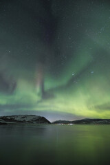 Fototapeta premium Magical Aurora Borealis in green, red, pink colours above Mortenhals with thousands of stars in the Troms region of Northern Norway