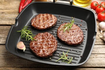 Pan with grilled patties, tomatoes and spices on wooden table, closeup
