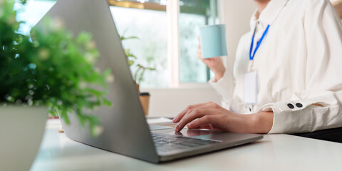 Remote worker enjoying coffee while typing on laptop in bright office