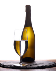 legant studio still life featuring a wine bottle and a clear glass placed on a textured slate mat against a bright white background. The minimalist backlit composition emphasizes the silhouette 