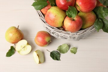 Fresh ripe apples with green leaves in wicker basket on white wooden table, above view