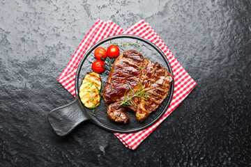 Delicious grilled beef steak with rosemary, zucchini and tomatoes on dark textured table, top view