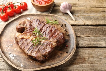 Delicious grilled beef steak with rosemary, spices and products on wooden table, closeup. Space for text