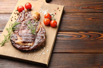 Delicious grilled beef steak with herbs, spices and tomatoes on wooden table, closeup. Space for text