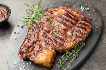 Delicious grilled beef steak with herbs, spices and ketchup on grey textured table, closeup