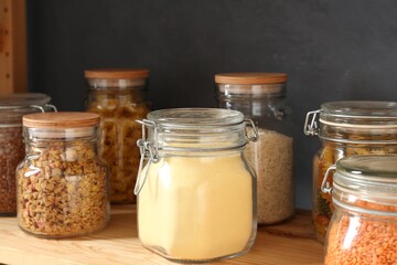 Glass jars with different products on wooden shelf, closeup