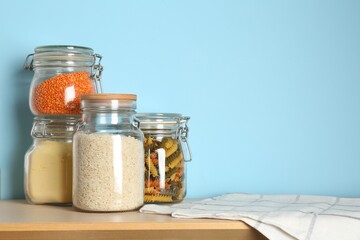 Glass jars with different products on wooden table against light blue background. Space for text