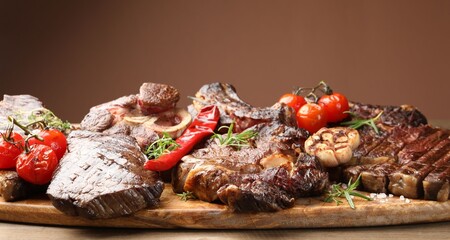 Pieces of tasty grilled beef with rosemary and vegetables on wooden table, closeup
