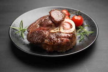 Tasty grilled beef steak served with rosemary, sauce and tomatoes on black wooden table