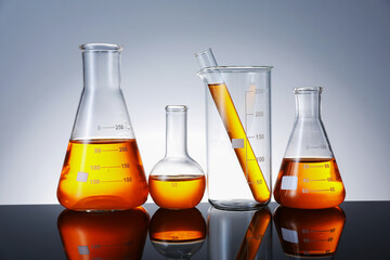 Different glassware with orange liquid on mirror surface against grey background