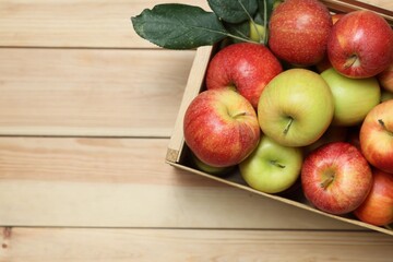 Fresh apples in crate and green leaves on wooden table, top view. Space for text