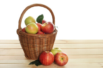 Fresh apples in wicker basket and green leaves on wooden table against white background
