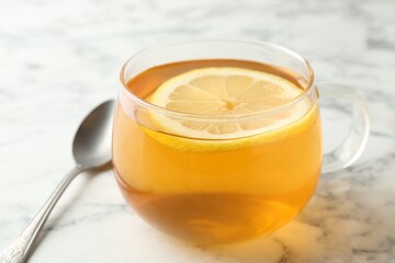 Aromatic tea with lemon in cup and spoon on white marble table, closeup