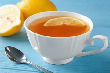 Aromatic tea in cup, lemons and spoon on light blue wooden table, closeup