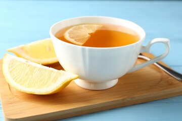 Aromatic tea in cup with lemon and spoon on light blue wooden table, closeup