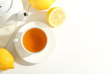 Aromatic tea in cup, lemons and teapot on white table, flat lay. Space for text
