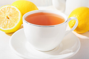 Aromatic tea in cup and lemons on white table, closeup